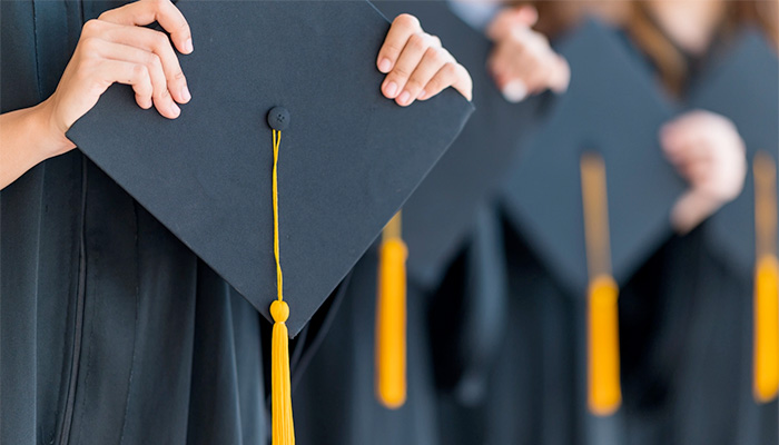 A row of students hold their graduation caps close to the camera.